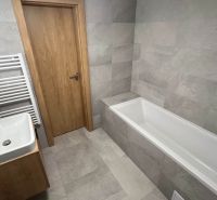 Fürdőszoba a rekreációs apartmanban káddal, mosdóval és szürke csempékkel.