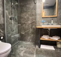 Fürdőszoba a nyaraló apartmanban sötét csempékkel és zuhanyzóval.