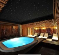 Luxusos wellness tér pezsgőfürdővel és nyugágyakkal, fával burkolva és dekoratív mennyezettel.