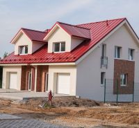 Családi ház Andócon piros tetővel és fehér garázskapukkal.