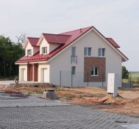 Családi ház Andódon piros tetővel, fákkal körülvéve és rendezett felhajtóval.