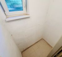 Kis szoba ablakkal, fehér falakkal és világos csempével egy kétszobás lakásban.