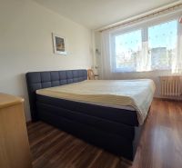 Hálószoba nagy ággyal, fa dekorációjú padlóval és ablakkal egy háromszobás lakásban.