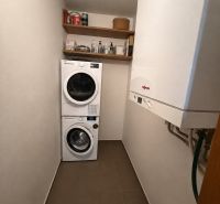 Mosókonyha egy háromszobás lakásban mosógéppel, szárítógéppel, polcokkal és gázkazánnal.