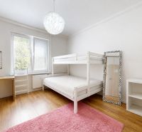 Gyerekszoba egy háromszobás lakásban emeletes ággyal, sárga székkel, polcokkal és fa dekorációjú padlóval.