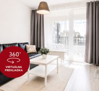 Nappali egy kétszobás lakásban fekete kanapéval, televízióval és erkéllyel.