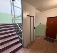 A társasházban lépcső, lift és egy háromszobás lakás ajtaja található.