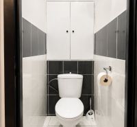 Fehér és szürke csempézett fürdőszoba, tárolóhely a WC fölött.