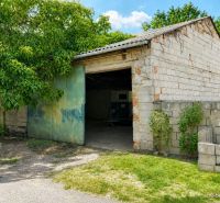 Az illmitzi családi ház téglából épült garázzsal rendelkezik, amelynek zöld ajtaja van, és körülötte zöld növényzet található.