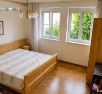 Hálószoba családi házban fa mintázatú padlóval, nagy ablakkal és ággyal.