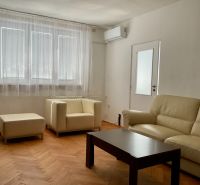 Nappali egy kétszobás lakásban krémszínű kanapéval és fa dekoros padlóval.