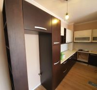 A Nyaraló apartman konyhája, ahol dominálnak a sötét szekrények és a fa dekorációjú padló.