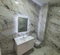 Fürdőszoba a nyaraló apartmanban márvány dekorációval és LED világítású tükörrel.