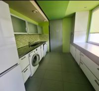 Konyha egy háromszobás lakásban mosógéppel, fehér bútorokkal és zöld falakkal.