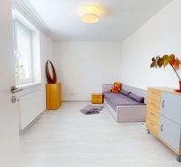 Szoba egy háromszobás lakásban kanapéval, komóddal és fa dekorációjú padlóval.