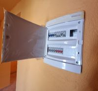 Elektromos elosztószekrény nyitott ajtókkal egy családi ház belső terében.