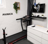 Fitnesz sarok futópaddal, televízióval és súlyzópadokkal egy háromszobás lakás pincéjében.