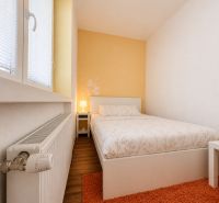 Hálószoba egy egyszobás lakásban fa mintázatú padlóval és narancssárga szőnyeggel.