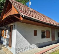 Családi ház Mikušovcén fa zsalugáterekkel és piros tetővel, zölddel körülvéve.