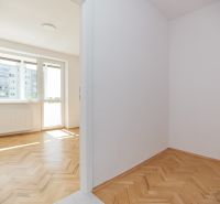 Világos szoba egy háromszobás lakásban, fa dekorációjú padlóval és nagy ablakkal.