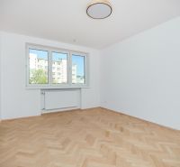 Szoba egy háromszobás lakásban fehér falakkal és fa mintázatú padlóval.