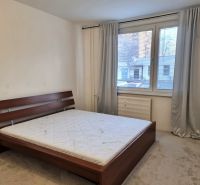 Hálószoba szürke függönyökkel, nagy ablakkal és ággyal egy kétszobás lakásban.