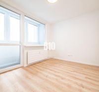 Tágas szoba egy háromszobás lakásban nagy ablakokkal és fa dekorációjú padlóval.