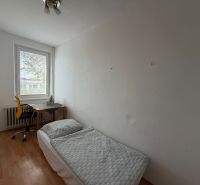 Szoba egy háromszobás lakásban ággyal, asztallal és fa dekorációjú padlóval.
