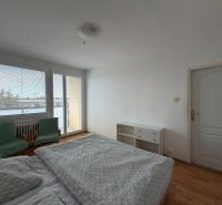 Hálószoba egy háromszobás lakásban, fa dekor padlóval, ággyal és székekkel.