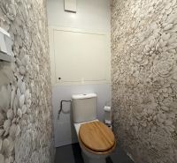 Virágmintás tapétával és fa ülőkével ellátott WC egy háromszobás lakásban.