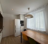 Konyha fehér hűtőszekrénnyel, színes székekkel és fa dekorációjú padlóval egy háromszobás lakásban.