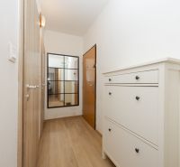 Keskeny folyosó fa dekor padlóval, tükörrel és fehér cipősszekrénnyel.