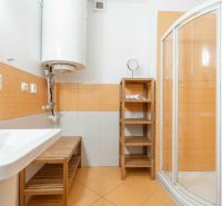 Fürdőszoba narancssárga csempékkel, zuhanyzóval és mosdóval egy nyaraló apartmanban.