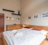 Világos hálószoba egy nyaraló apartmanban, fa dekoros padlóval és egyszerű berendezéssel.