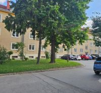 Parkoló a háromszobás lakásoknál a Trnava-i Študentská utcán, zölddel és fákkal körülvéve.