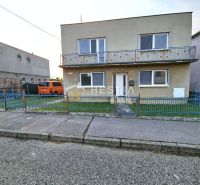 Családi ház Szenicén erkéllyel, kék kerítéssel és parkoló autóval.