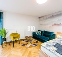 Stílusos nyaraló apartman fa hatású padlóval, kanapéval és növényekkel.