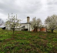 Gyártóhelyiségek Leseniceben virágzó fákkal és zöld fűvel körülvéve.