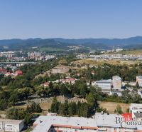 Kilátás Besztercebánya panorámájára a Komenského utcáról, láthatók családi házak és a természet.