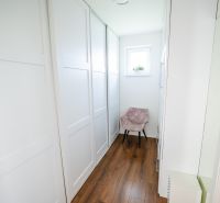 Keskeny folyosó egy családi házban, fa mintázatú padlóval és ablakkal.