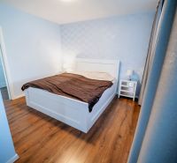 Hálószoba családi házban ággyal, éjjeliszekrényekkel és fa mintázatú padlóval.