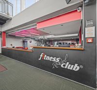 Egy fitnesz klub recepciója felirattal, piros világítással és dekoratív trófeákkal zöld árnyalatú padlón.
