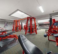 Fitneszközpont erősítő gépekkel és piros padokkal, alkalmas üzlethelyiségek.