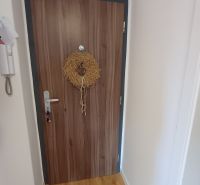 Bejárati ajtó egy kétszobás lakásban koszorúval és fa dekorációjú padlóval.