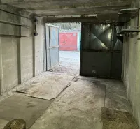 Betongarázs nyitott acélajtókkal, kilátás egy másik garázsra kívül.