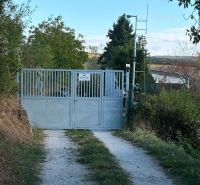 A Banka-i házhoz vezető kapu, amelyet zöld növényzet és földút vesz körül.