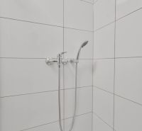 Zuhanykabin fehér csempékkel és zuhanyfejjel a garzonlakásban.