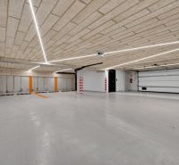 Beton mennyezetű és padlójú parkológarázs, lineáris lámpatestekkel megvilágítva.