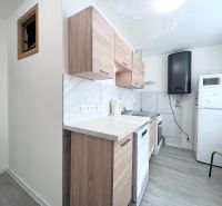 Konyha egy háromszobás lakásban, fa mintázatú padlóval és fehér háztartási gépekkel.