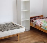 Két ágy, polc és fa dekorációjú padló egy kétszobás lakásban.
